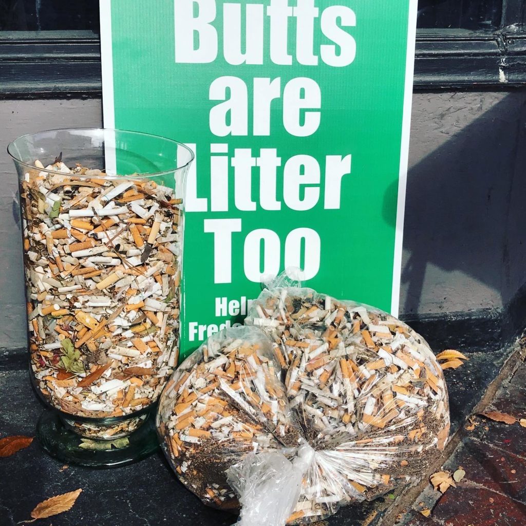 "Butts are litter too" sign next to a bag of littered cigarette butts
